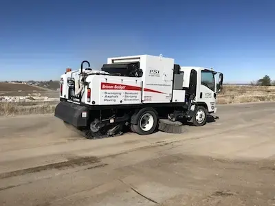 Broom truck sweeping dirty road.